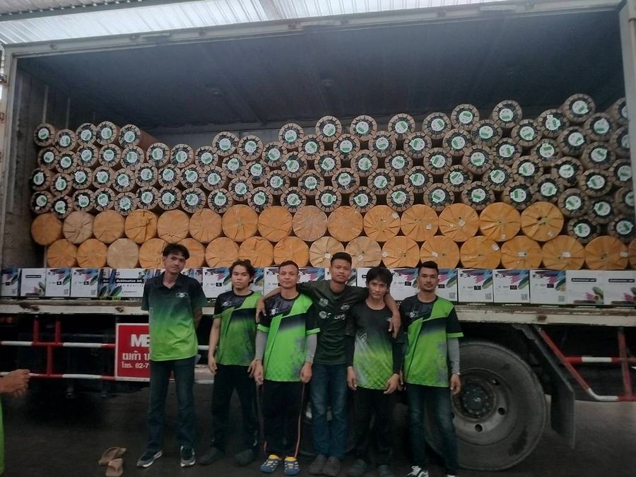 A group of people standing in front of a truck stacked with roll materials